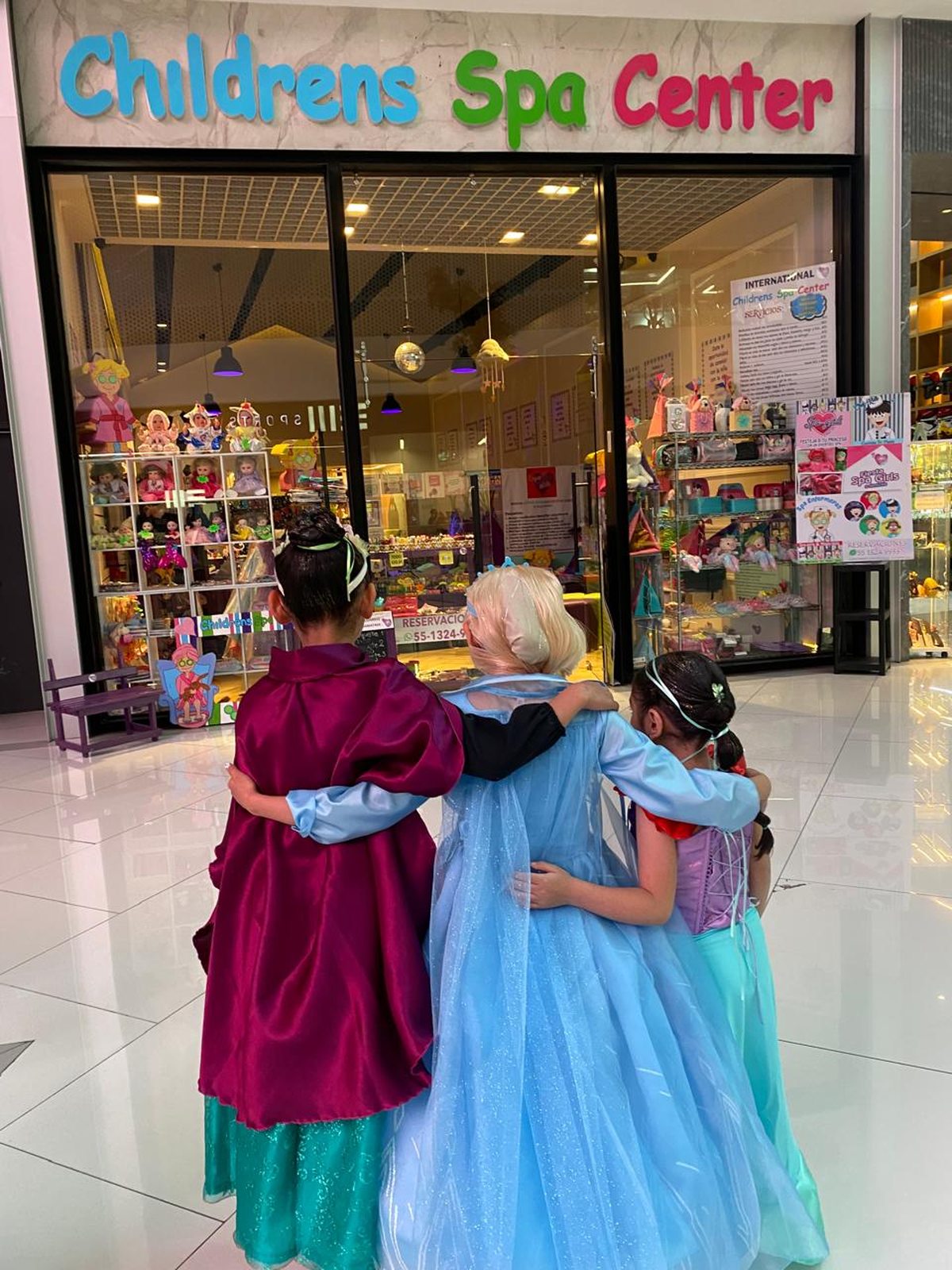 Tres niñas con vestido de princesa abrazadas frente a Childrens Spa Center